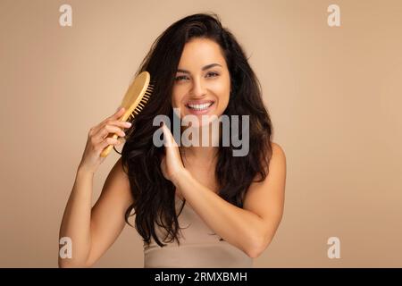 Cheerful indian woman combing beautiful dark long hair, studio background Stock Photo