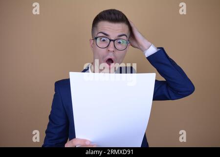 Shocked Young Handsome Elegant Man Holding His Head While Reading Documents on Isolated Background Stock Photo