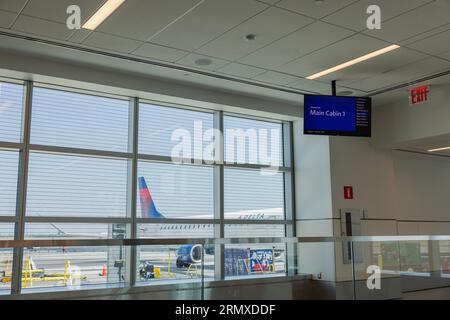 View of invitation board at airport for main cabin passengers going on board with view of parked Delta aircraft from inside airport through window. US Stock Photo