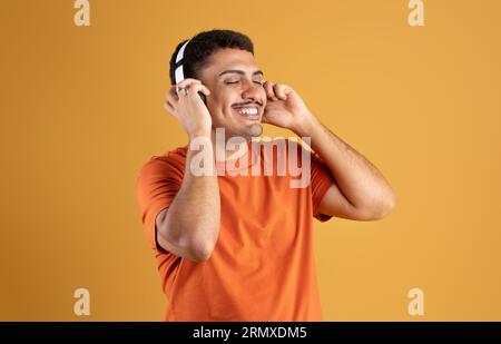 Carefree brazilian man enjoy listening to music with closed eyes and smiling, using modern wireless headphones Stock Photo