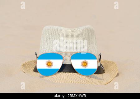 Sunglasses with glasses in form of flag of Argentina and a hat lie on sand. Concept of summer holidays and travel in Argentina. Summer rest Stock Photo