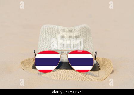 Sunglasses with glasses in form of flag of Thailand and a hat lie on sand. Concept of summer holidays and travel in Thailand. Summer rest Stock Photo