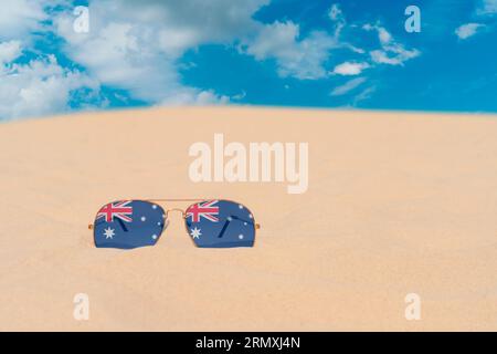 Sunglasses with glasses in form of flag of Australia lie on sand against blue sky. Concept of summer holidays, travel and tourism in Australia Stock Photo