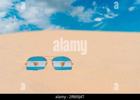 Sunglasses with glasses in form of flag of Argentina lie on sand against blue sky. Concept of summer holidays, travel and tourism in Argentina Stock Photo
