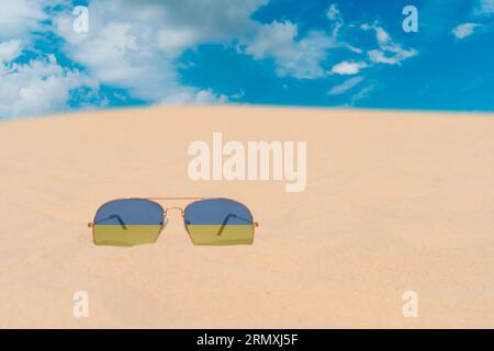 Sunglasses with glasses in form of flag of Ukraine lie on sand against blue sky. Concept of summer holidays, travel and tourism in Ukraine Stock Photo