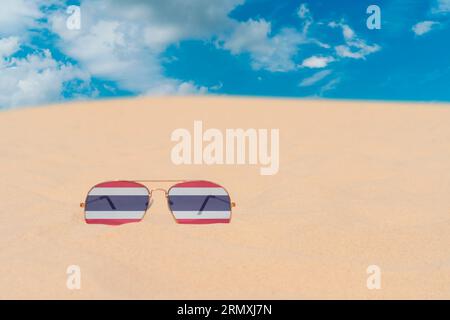 Sunglasses with glasses in form of flag of Thailand lie on sand against blue sky. Concept of summer holidays, travel and tourism in Thailand Stock Photo