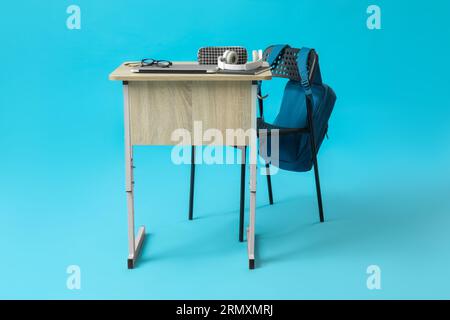 Modern school desk with backpack, laptop and stationery on blue background Stock Photo