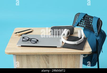 Modern school desk with backpack, laptop and stationery on blue background Stock Photo