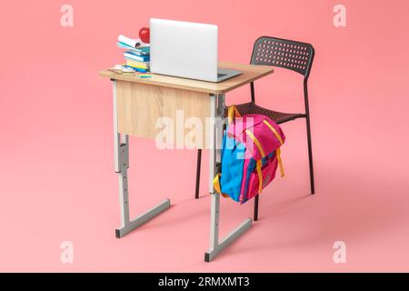 Modern school desk with backpack, laptop and stationery on pink background Stock Photo