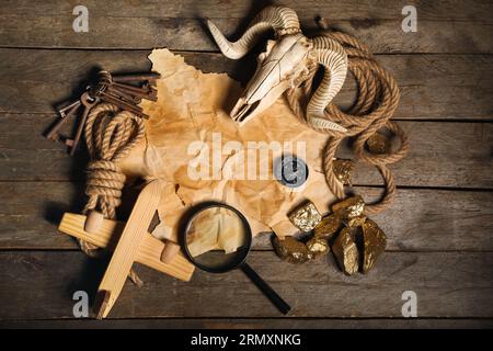 Skull of sheep with travel equipment, treasure map and golden nuggets on brown wooden background Stock Photo