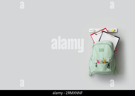 Stylish school backpack with stationery hanging on light wall Stock Photo
