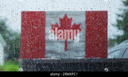 Raindrops on a window looking out at a wooden Canadian Flag on a very rainy day. Stock Photo