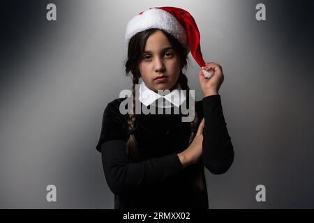 Portrait of little girl with Wednesday Addams costume. Wednesday girl with a Santa hat Stock Photo