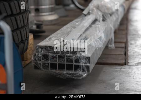 A lot or bunch of aluminium profiles bound together, destined for laser cutting. Batch or pack of aluminium square tubing on the floor. Stock Photo