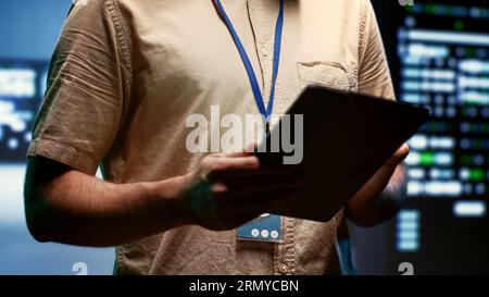 Engineer doing annual maintenance, helping extend data center hardware life span and avoiding downtime. Expert monitoring server infrastructure components using tablet, close up Stock Photo