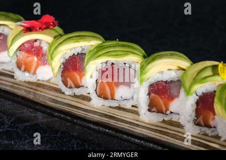 High angle of delicious Japanese uramaki sushi rolls with avocado slices on top served on tray in daylight on blurred black surface Stock Photo