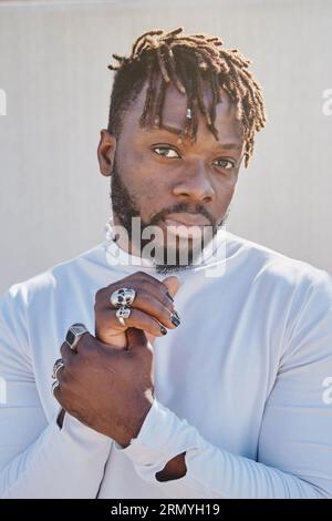 Portrait of thoughtful bearded African American man with dreadlocks wearing rings on fingers and looking at camera Stock Photo