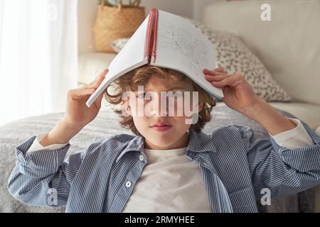 Upset preteen child in casual clothes looking at camera and frowning while staying home and doing homework in living room during COVID19 epidemic Stock Photo