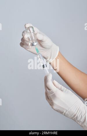 Hands of crop unrecognizable doctor in protective gloves drawing up vaccine from vial into syringe against white background in room Stock Photo