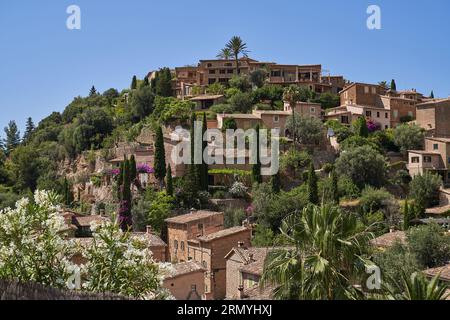 Picturesque view of Deia town with houses and tropical green trees under blue sky on sunny summer day in Spain Stock Photo