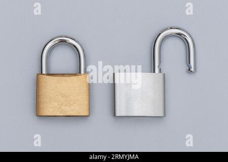 Locked golden and unlocked silver padlock on the gray background. Stock Photo