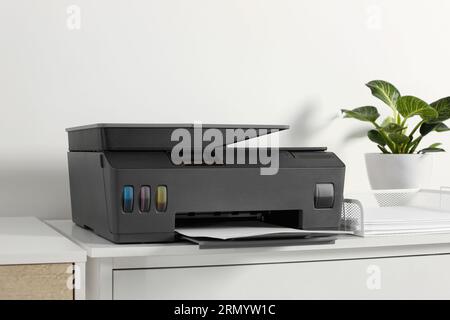 Modern printer with paper on chest of drawers indoors Stock Photo