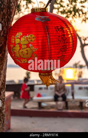 The setting sun shines through thin material of the lantern,from across the Mekong river,hanging from a tree,to be lit up after dark. Stock Photo