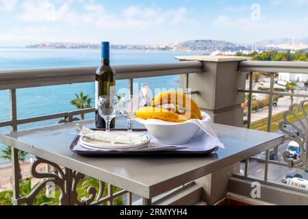 View from a hotel balcony of a bottle of wine, two wine glasses and a bowl of fruit, along the Athenian Riviera near Piraeus in Palaio Faliro, Greece. Stock Photo