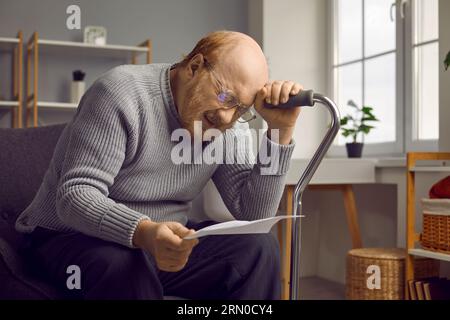 Depressed disappointed elderly man reading bad news from paper document or letter. Stock Photo
