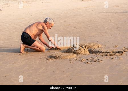 Calangute, Goa, India - January 2023: An elderly Caucasian man building a sand castle on the beach. Stock Photo