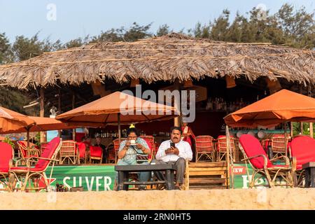 Calangute, Goa, India - January 2023: Two Indian tourists sitting at beach shack at the popular beach in Calangute. Stock Photo