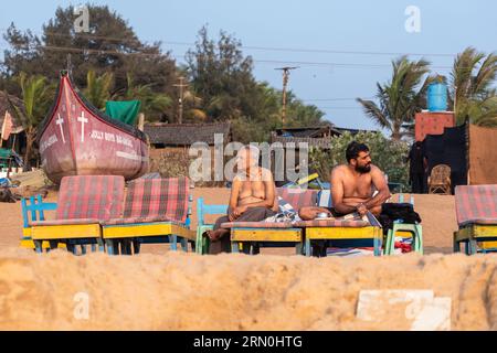 Calangute, Goa, India - January 2023: Two Indian men getting a tan on a sub bed at a beach shack. Stock Photo