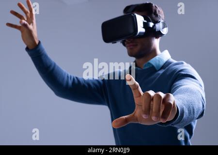 Biracial businessman using vr headset and pointing with fingers on grey background Stock Photo