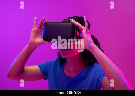 Biracial woman using vr headset on neon pink to purple background Stock Photo