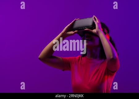 Biracial woman using vr headset on neon pink to purple background Stock Photo