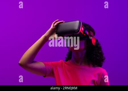Biracial woman using vr headset on neon pink to purple background Stock Photo