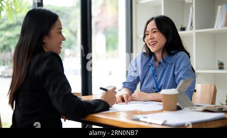 An attractive and cheerful young Asian businesswoman or female financial consultant enjoys talking with her client during the an informal meeting in t Stock Photo