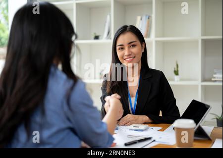 A gorgeous and professional Asian businesswoman is shaking hands with a female client or colleague in the office after an informal meeting. Stock Photo