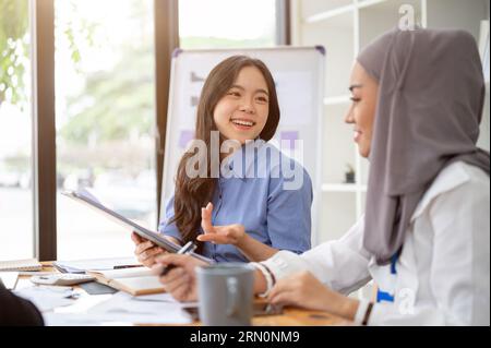A friendly and charming young Asian businesswoman is talking with her colleague while working on a project together in the office. Stock Photo