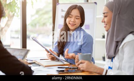 A cheerful and confident young Asian businesswoman is sharing her ideas with her team during the meeting, brainstorming and planning a project togethe Stock Photo