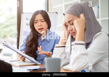 A dissatisfied and serious Asian businesswoman is complaining about the project's mistakes to her Muslim employee or colleague during the meeting. Stock Photo