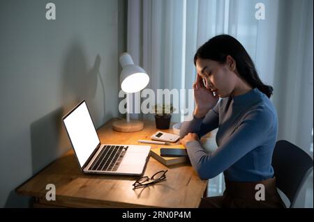 A tired and sleepy young Asian female college student is falling asleep while doing homework at a table in her room in the evening. A white screen lap Stock Photo