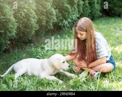 Little girl playing with a golden retriever puppy in the garden. Friends at home. Stock Photo