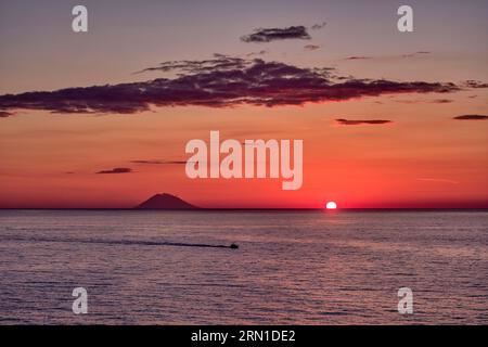 The sun sets over the water near the volcanic island of Stromboli, seen from Tropea. Stock Photo