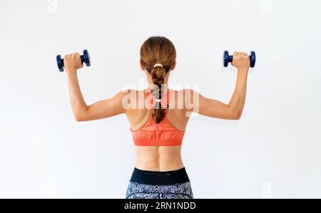 Rear view of sporty female athlete holding dumbbells in her hands. Stock Photo