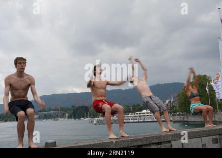 Three young men and one woman are bouncing off from a bridge to jump backwards to Lake Zurich. Stock Photo