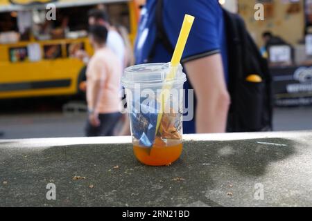 Plastic glass with orange drink, straw and small pieces of wrappers from chocolate lying on table as garbage. Stock Photo