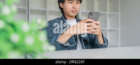 Asian man feels relax with using smartphone texting online and scrolling news feed in social media application on his desk at home Stock Photo