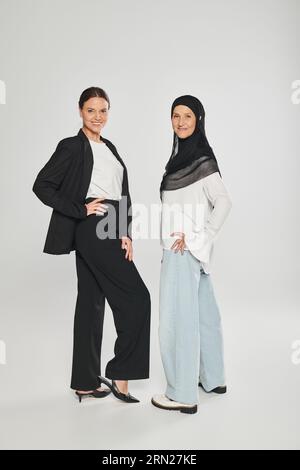 full length of smiling businesswoman and woman in hijab posing on grey background Stock Photo