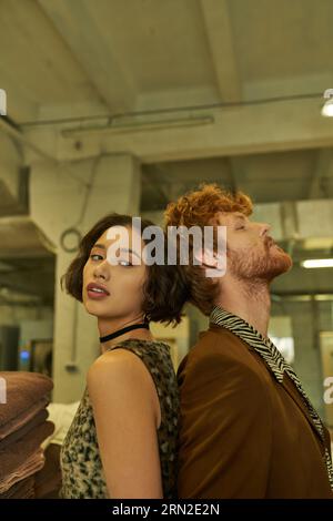 stylish young interracial couple standing back to back in public laundry Stock Photo